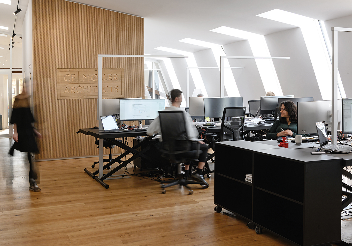 Großraumbüro von C.F. Møller Architects mit Holzwand und Arbeitsplätzen unter Dachfenstern