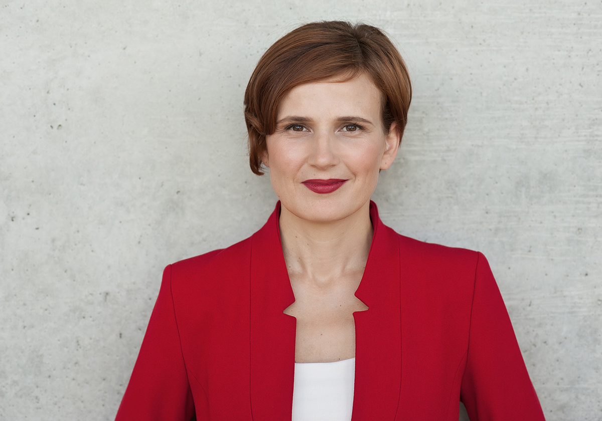 Katja Kipping im roten Blazer vor einer Betonwand