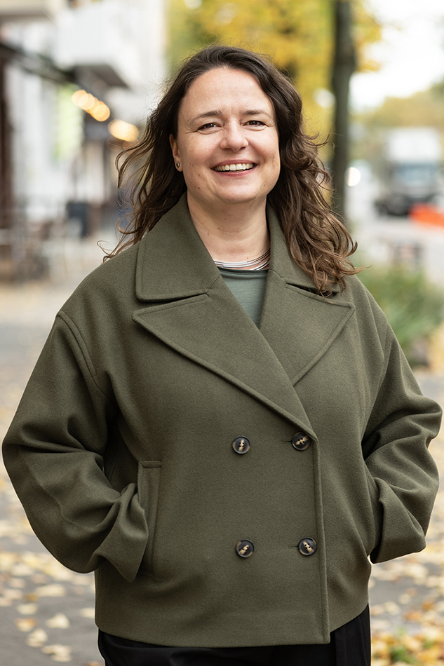 Susann Belitz im grünen Mantel auf einer herbstlichen Straße