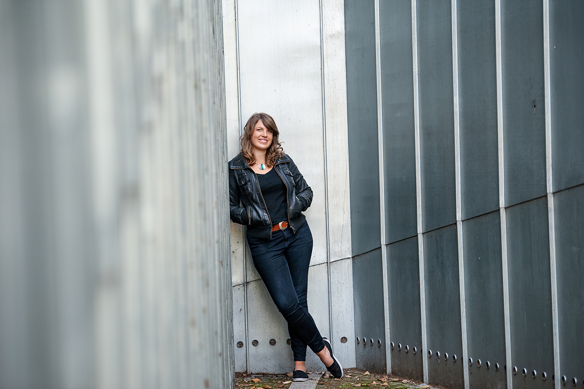Franca Parianen in Lederjacke, angelehnt an eine Wand zwischen hohen Metallfassaden