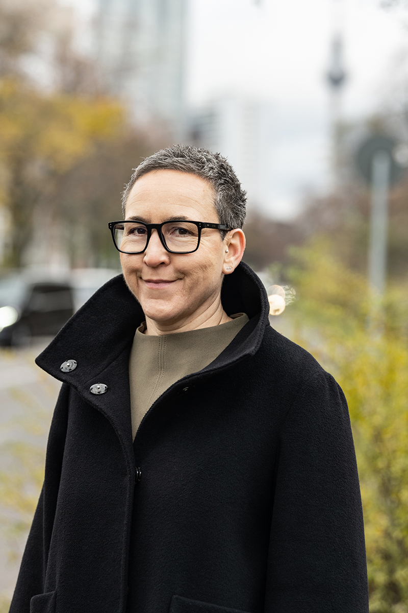 Julia Fernández-Pola mit Brille im schwarzen Mantel, im Hintergrund der Berliner Fernsehturm