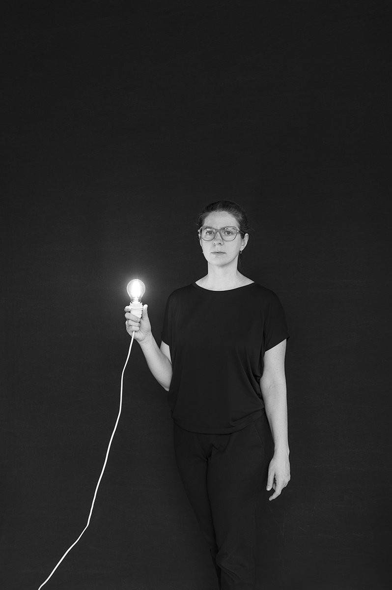 Schwarz-Weiß-Porträt von Paula Longato, die eine leuchtende Glühbirne an einem Kabel hält