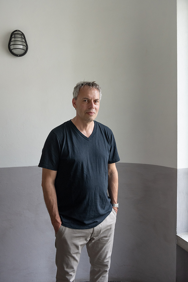 Porträt eines Mannes im dunklen T-Shirt vor einer zweifarbig gestrichenen Wand