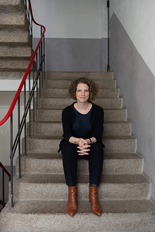 Porträt einer Frau mit Locken, die auf einer Granittreppe mit rotem Geländer sitzt